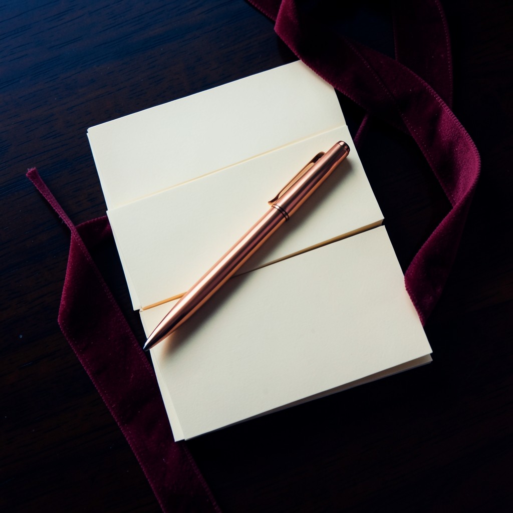 Blank ivory cards lined up on dark wood with a copper pen